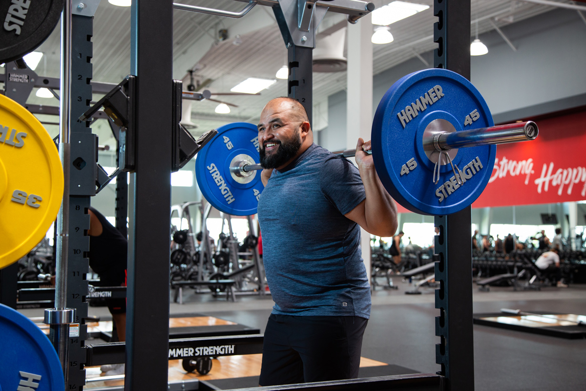 A man at a VASA gym smiling while squatting