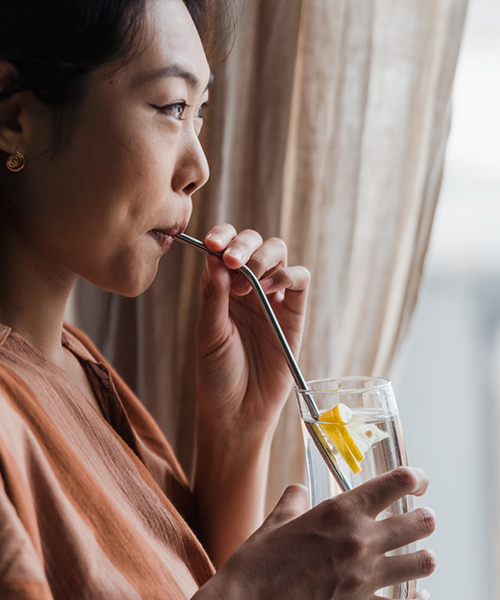 An Asian lady drinking lemon water from a straw