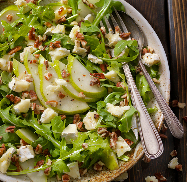 a bowl full of salad with fresh cut pears on top for a healthy meal.