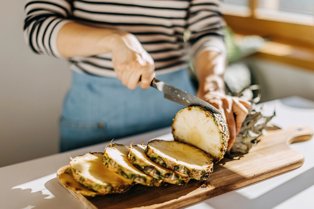 Female cutting pineapple in kitchen on cutting board