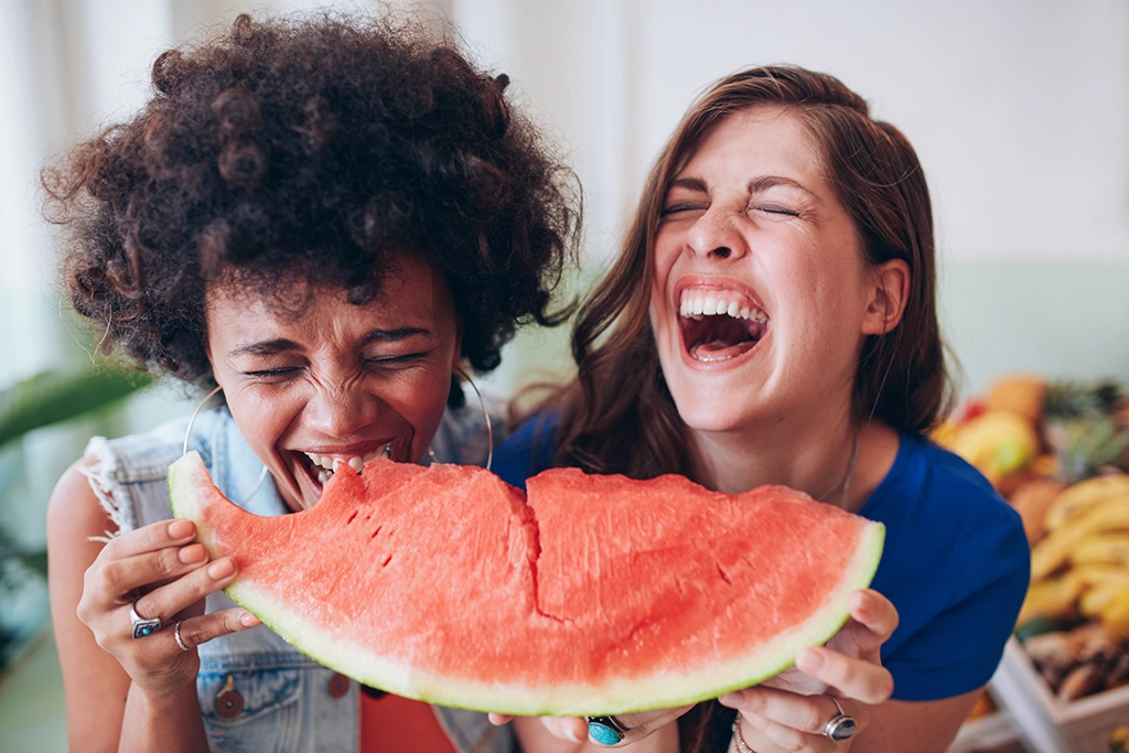 Two female friends laughing and eating a watermelon together