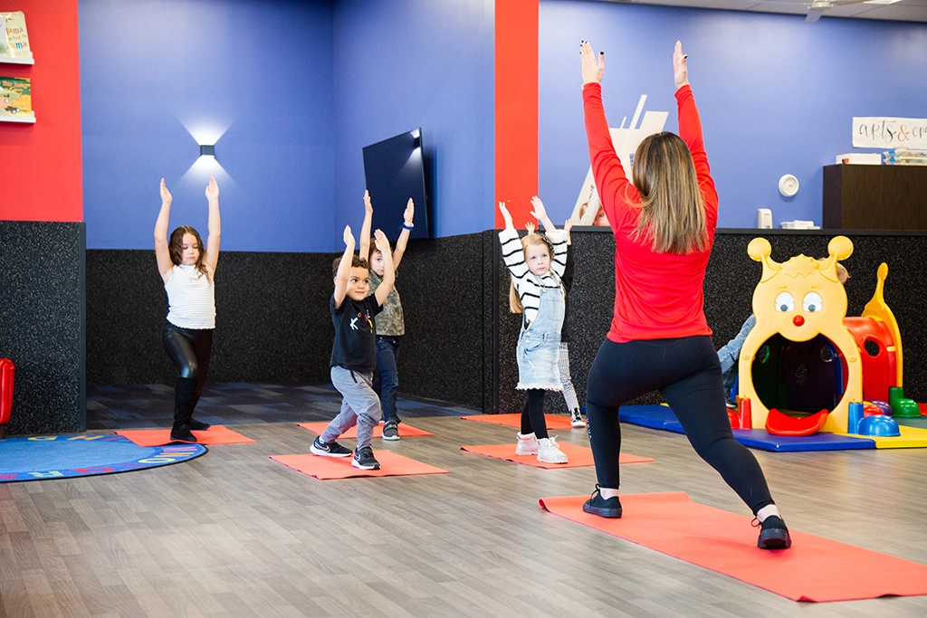 Female VASA employee leading children in a yoga stretch exercise