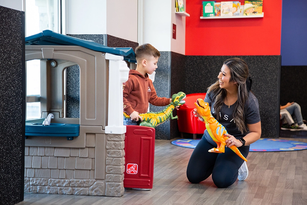 Female VASA employee entertaining a male child with dinosaur toys in VASA Fitness KidCare