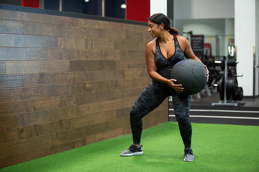 Female athlete exercising with a medicine ball on turf at VASA Fitness