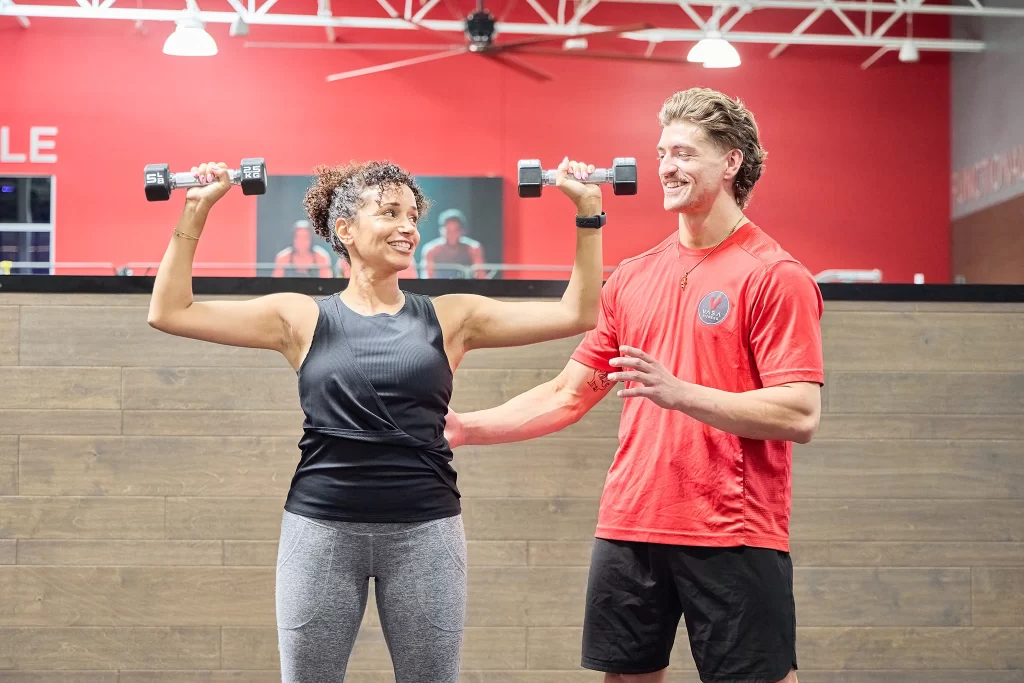 Female athlete lifting dumbbells with a male personal trainer at VASA Fitness