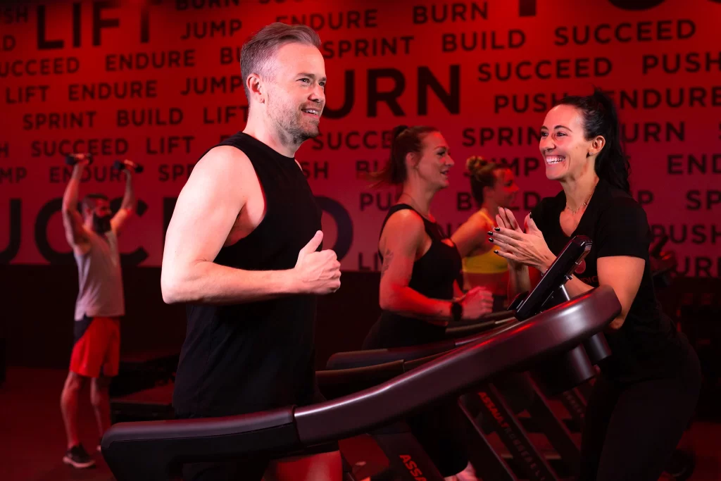 Male athlete running on a treadmill in STUDIO RED getting support from a female personal trainer at VASA Fitness